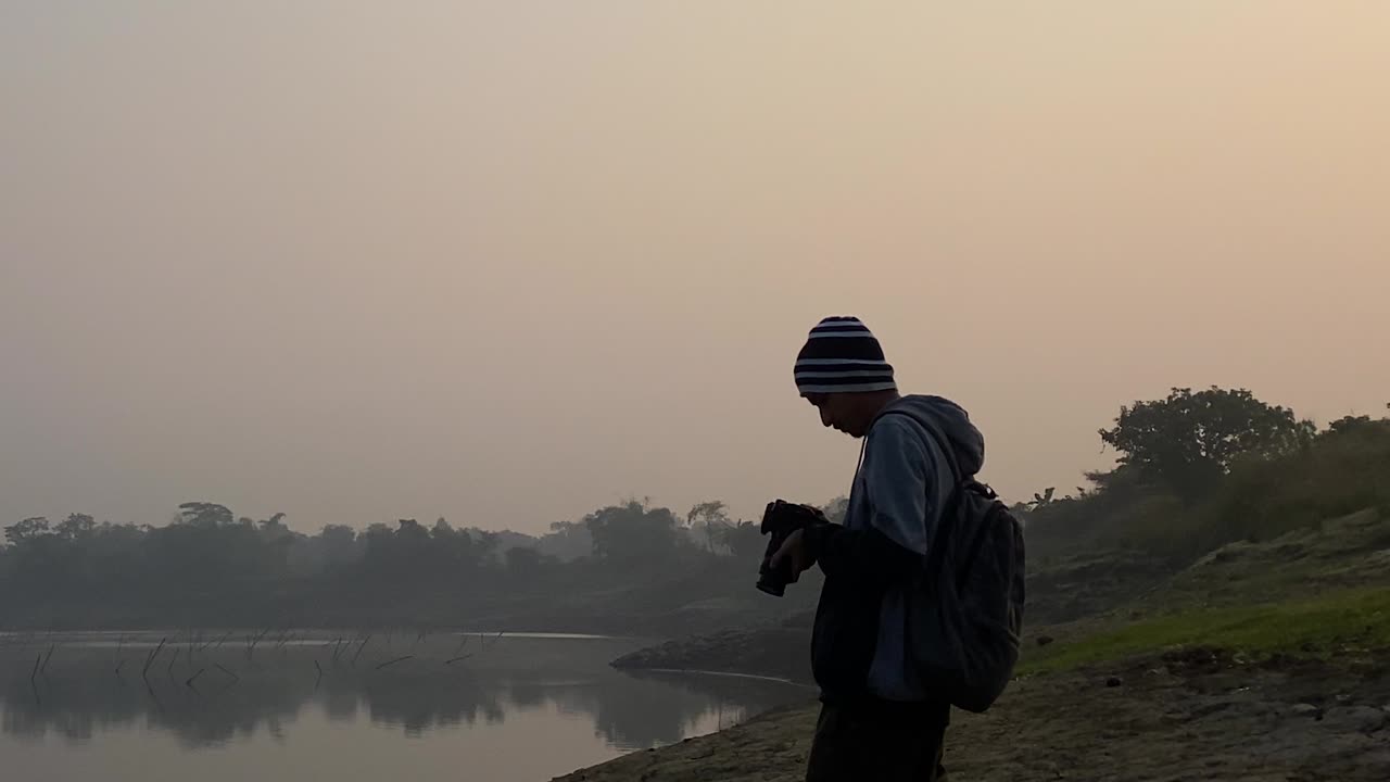 Potret Close-up seorang Fotografer yang Memotret lalu Melihat Layar di Tepi Sungai