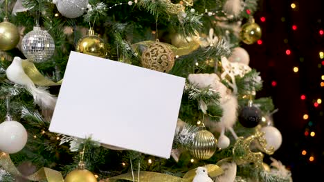 hand put white paper card note on decorated christmas tree with blinking lights