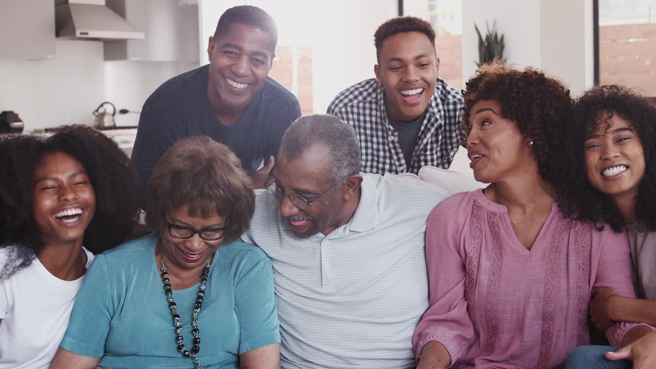 Multi generation black family sit relaxing together at home smiling to camera, close up