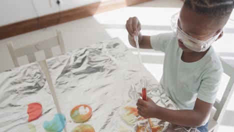 African-american-boy-sitting-at-table-holding-test-tubes-with-liquid,-in-slow-motion