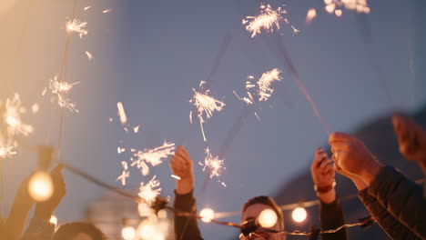 Fröhliche-Gruppe-Von-Freunden-Hält-Wunderkerzen-In-Der-Hand-Und-Feiert-Silvester-Auf-Dem-Dach-In-Der-Nacht.-Sie-Haben-Spaß-Beim-Tanzen-Und-Genießen-Die-Feiertagsfeier.-Verschiedene-Junge-Leute-Winken-Mit-Festlichen-Feuerwerken