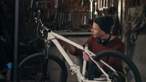 mastering the details: skilled mechanic in brown sweater inspecting white bike in workshop