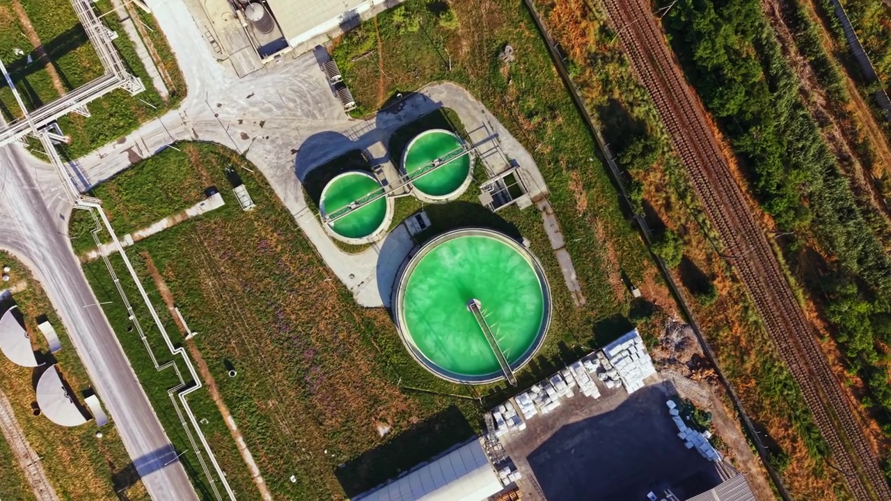 Green tanks are used in a processing plant for water treatment and environmental management near a railway in an industrial area