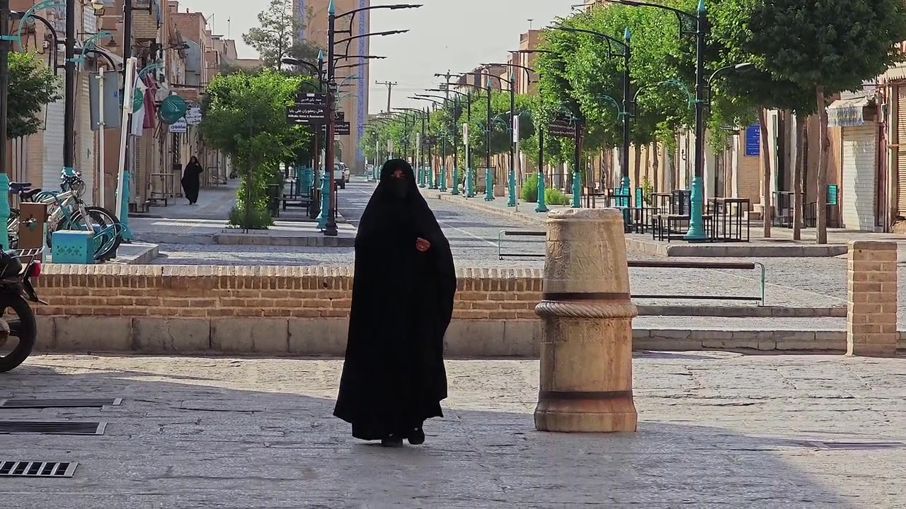 Tarihi bir İran sokağında çadurlu kadın yürüyor.