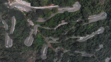 Hairpin-bends-in-Yercaud,-India-covered-with-endless-vast-forest-with-trees-growing-rapidly-vehicles-passing-on-the-road-top-view