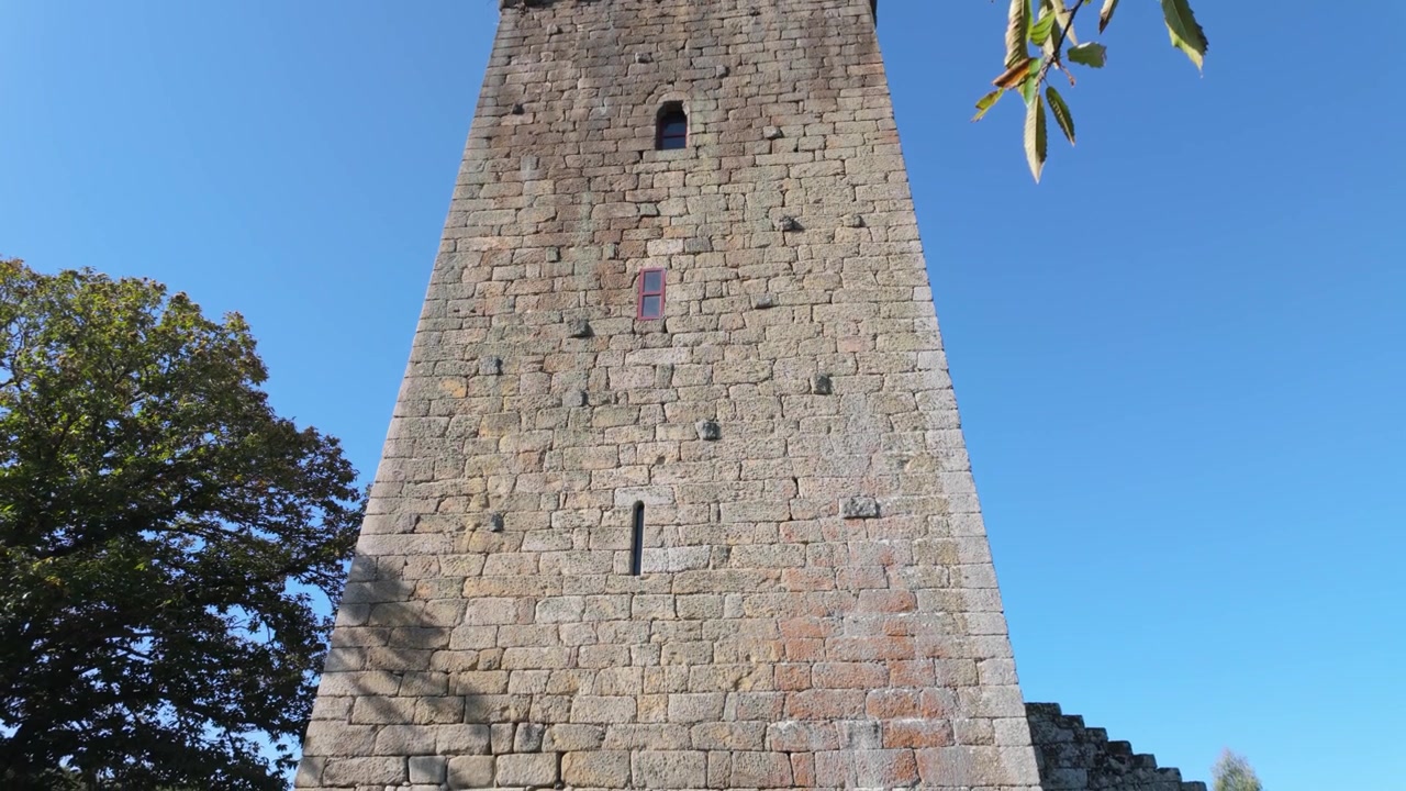 Vista dal basso della medievale Torre de A Forxa a Porqueira, Ourense, una storica torre difensiva in pietra che si erge sopra il paesaggio rurale di A Limia in Galizia, Spagna nord-occidentale, sotto cieli sereni.