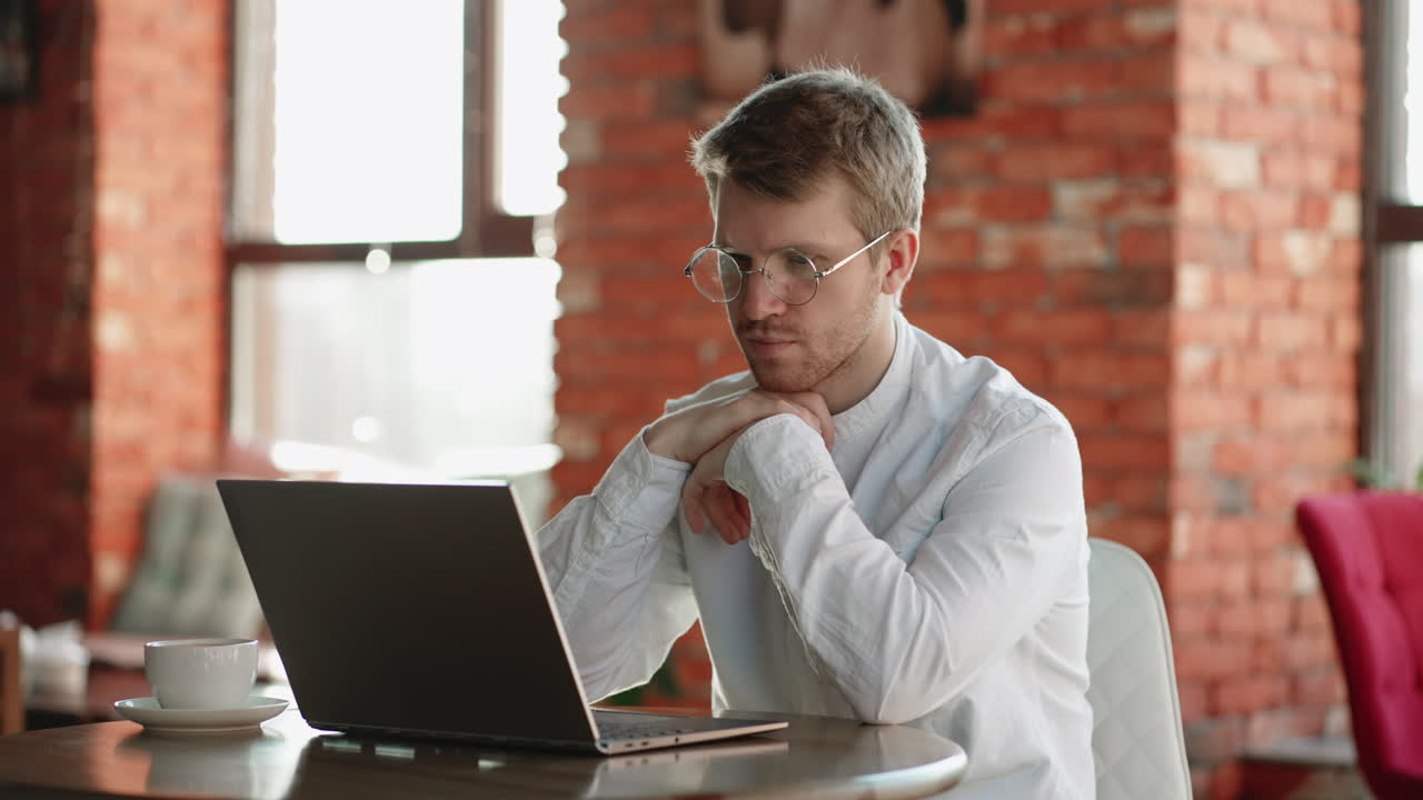 un hombre pensativo está leyendo noticias en internet y pensando usando una computadora portátil en una cafetería durante la pausa para el café