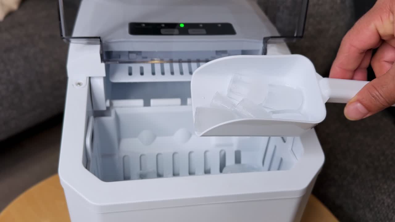 Close-up of a hand using a scoop to pick bullet ice cubes from an ice maker. Clean, modern indoor shot ideal for appliance B-roll, lifestyle content, or kitchen sequences