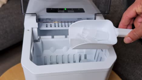 close-up of a hand using a scoop to pick bullet ice cubes from an ice maker. clean, modern indoor shot ideal for appliance b-roll, lifestyle content, or kitchen sequences