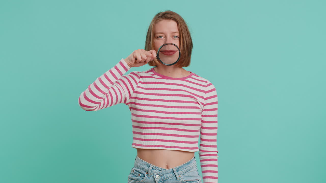 Woman holding magnifier glass loupe on teeth looking at camera showing funny smiling face mouth