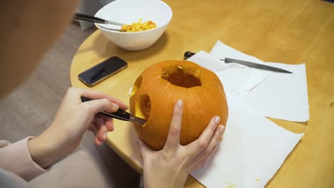 primer plano de una mujer tallando calabaza naranja en casa para halloween