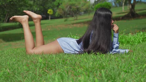 a young east indian girl in a blue shirt at a park laying in the grass