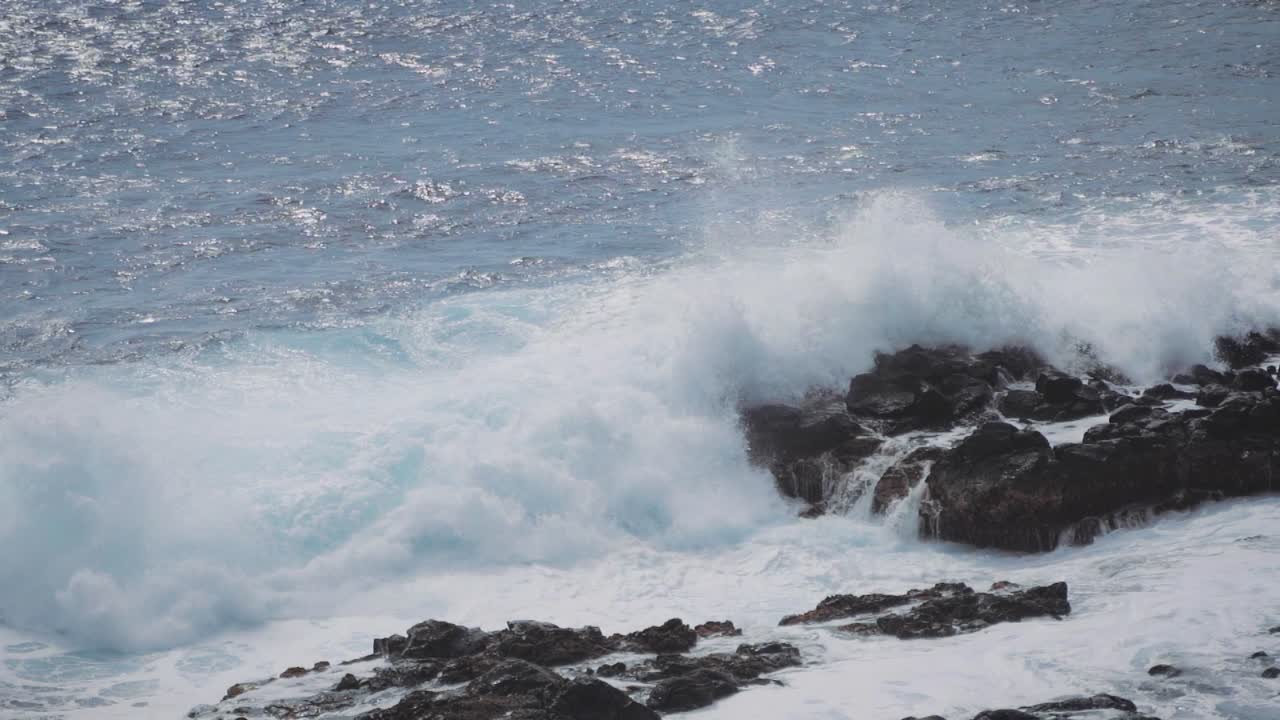 A big wave crashing in off the coast of Hawaii on to some rocks.
