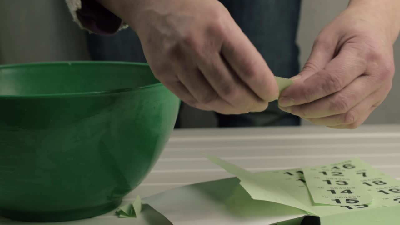Hands folding lottery tickets and putting into bowl for draw medium shot