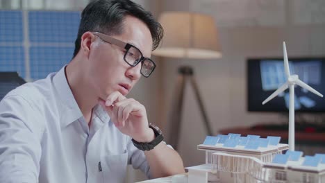 close up of unsatisfied asian man looking at model of a small house with solar panel