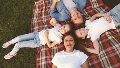 top view of happy family lying on blanket in park, laughing and having fun together