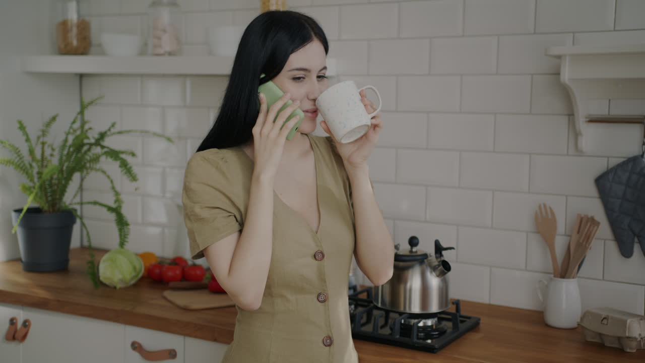 Woman Talking on Phone and Drinking in Kitchen