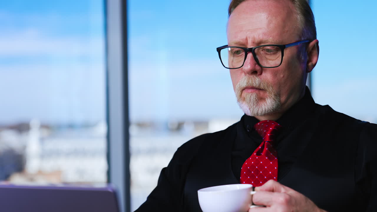 Adult Caucasian confident man looking focused on laptop typing on it. Man finishes work, closes computer, sighs with relief and drinks coffee. Close up.