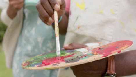 mid section of senior african american couple painting on wooden easel in garden, slow motion