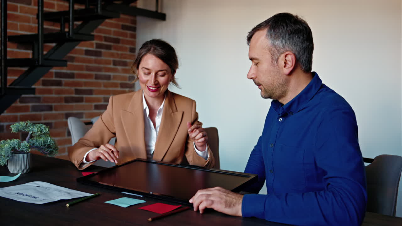 Man and woman discussing plans on a screen at the table, in an office