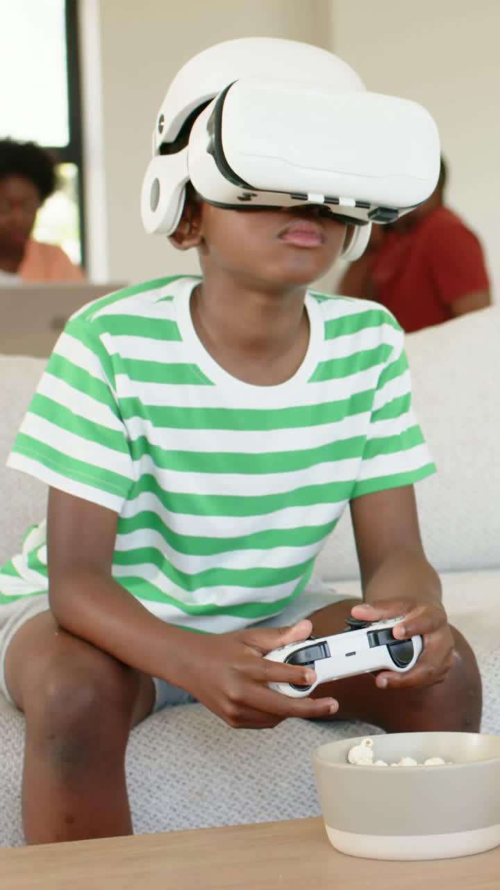 Vertical video: VR game starting, kid in green tee leaning, holding gamepad on couch, white headset