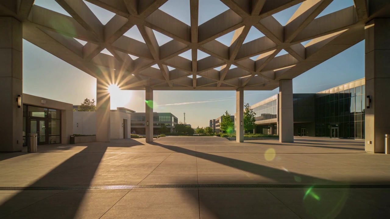 Dossel e colunas projetando sombras mutáveis pela praça, o sol baixo se movendo e criando um efeito de flare na lente.
