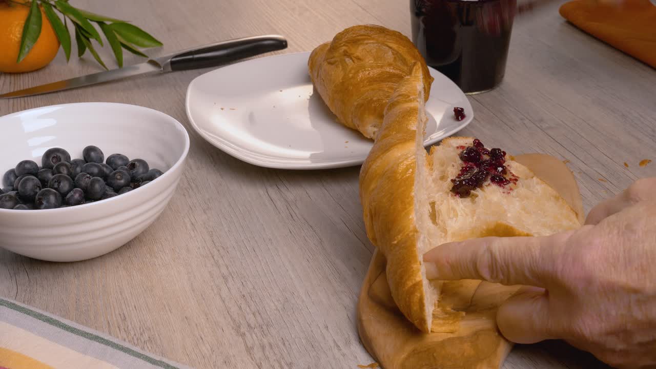 un hombre pone mermelada de arándanos en croissants en una tabla de cortar de madera.