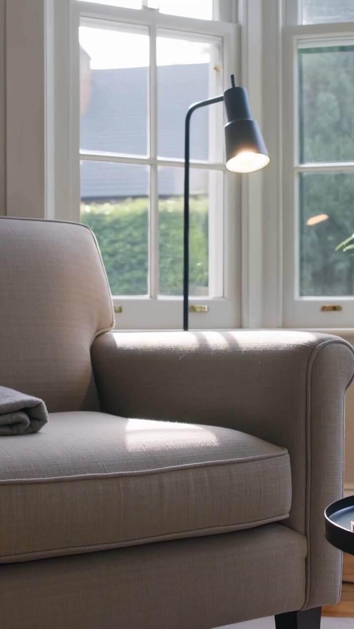 Vertical video: Panning camera revealing beige armchair in living room, capturing sun and blanket