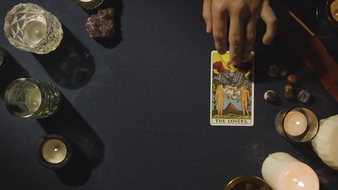 toma aérea de una persona que da una lectura de cartas del tarot colocando la carta de los amantes en la mesa 1