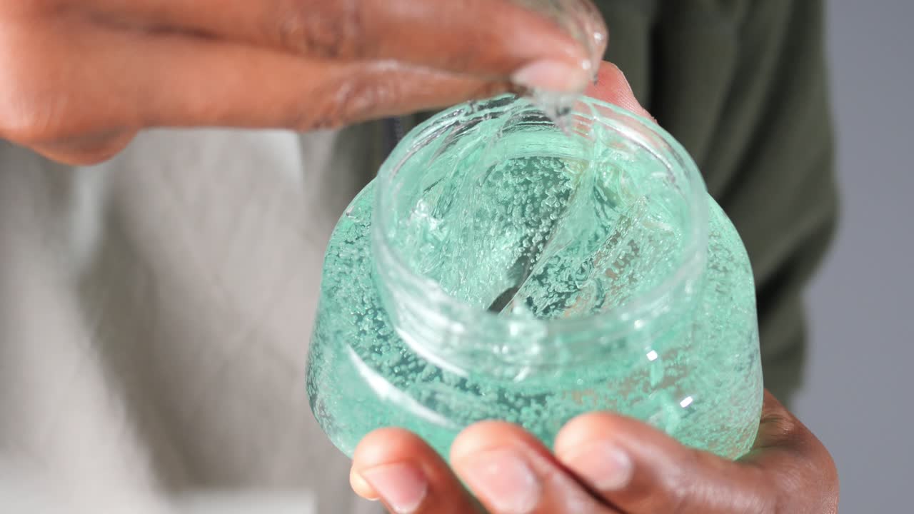 Primer plano de mano recogiendo gel verde de un frasco
