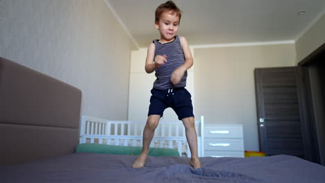 lovely caucasian toddler lies on his belly on the bed. beautiful smiling kid stands up and jumps on the bed.