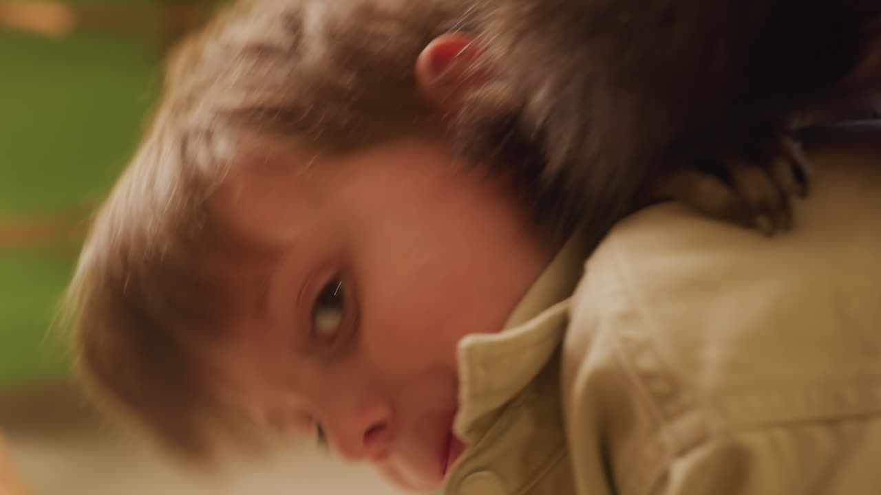Procione sulla spalla di un bambino caucasico, delicatamente appollaiato in una luminosa stanza dei giochi al chiuso; un procione curioso esplora i capelli e il colletto mentre il giovane sembra sorpreso e gentile; primo piano delle zampe, della pelliccia e degli occhi