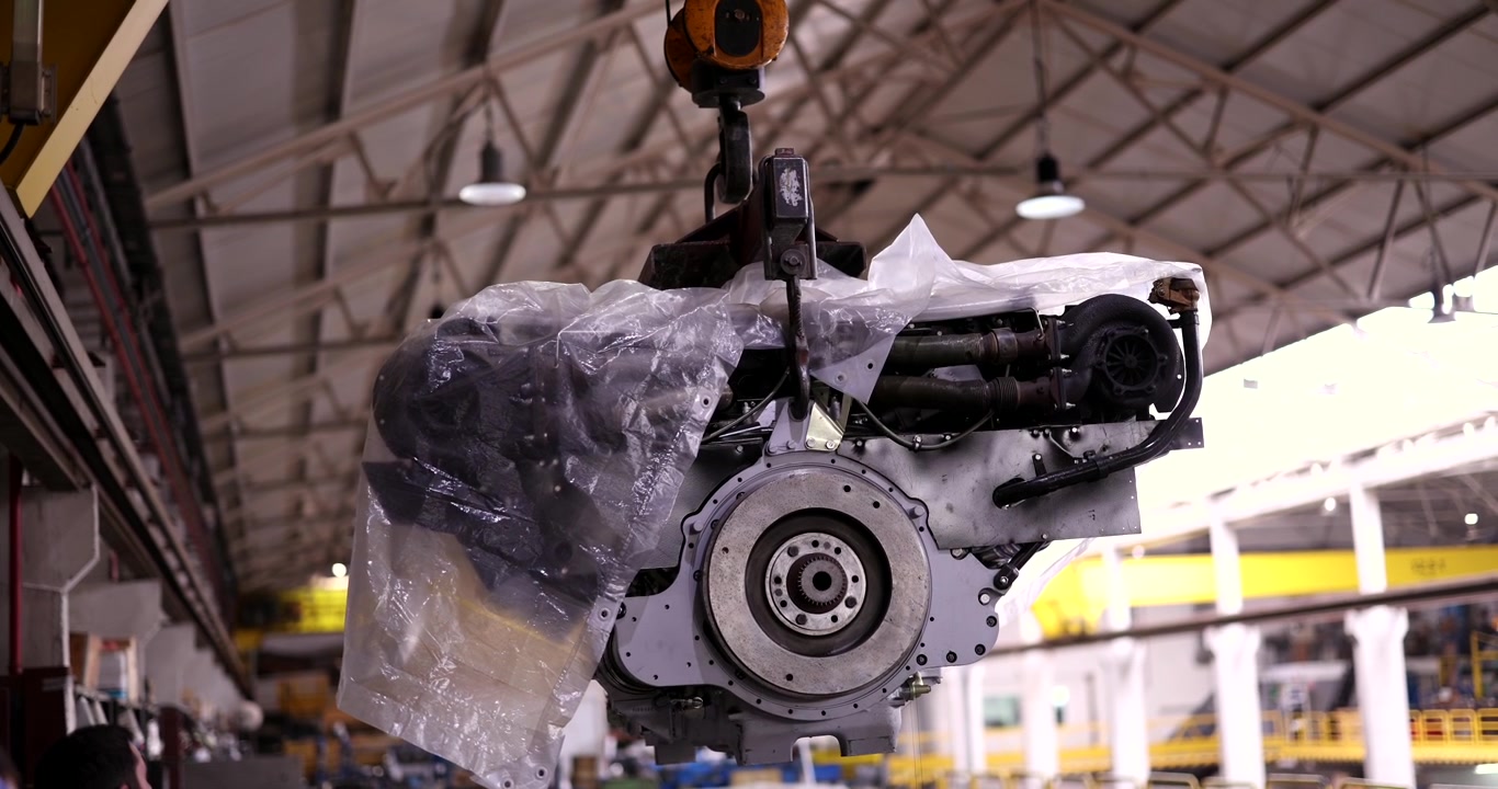 Grande motore industriale sospeso da una gru in uno stabilimento di produzione