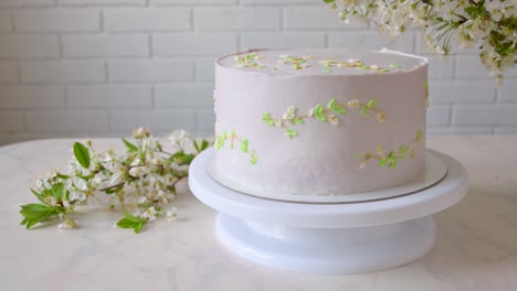 delicate pink cake is spinning on a stand. spring twigs with white flowers