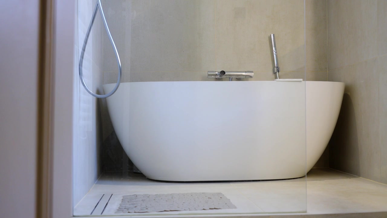 Modern white bathtub in a minimalist bathroom with neutral walls and glass panel