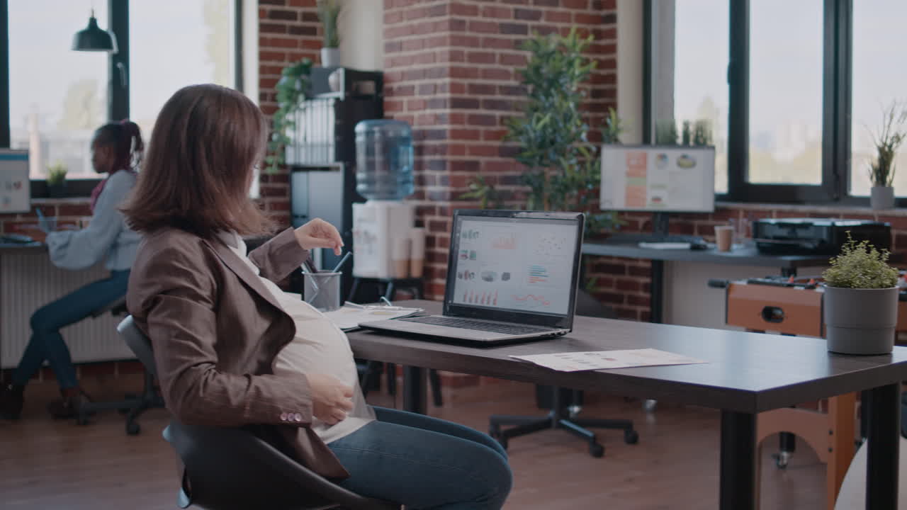 Pregnant business woman working on laptop using documents for marketing strategy