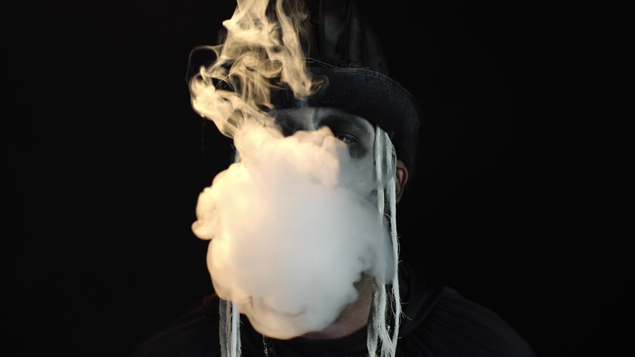 зловещий человек с макияжем на хэллоуин, выдыхающий сигарету, курящий из рта и улыбающийся