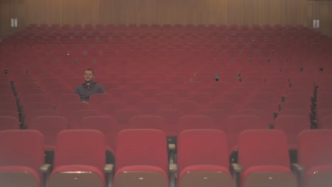 a tall white guy is in an empty theatre. he is the only one watching the comedy show and he starts to laugh while he enjoys what he sees on stage