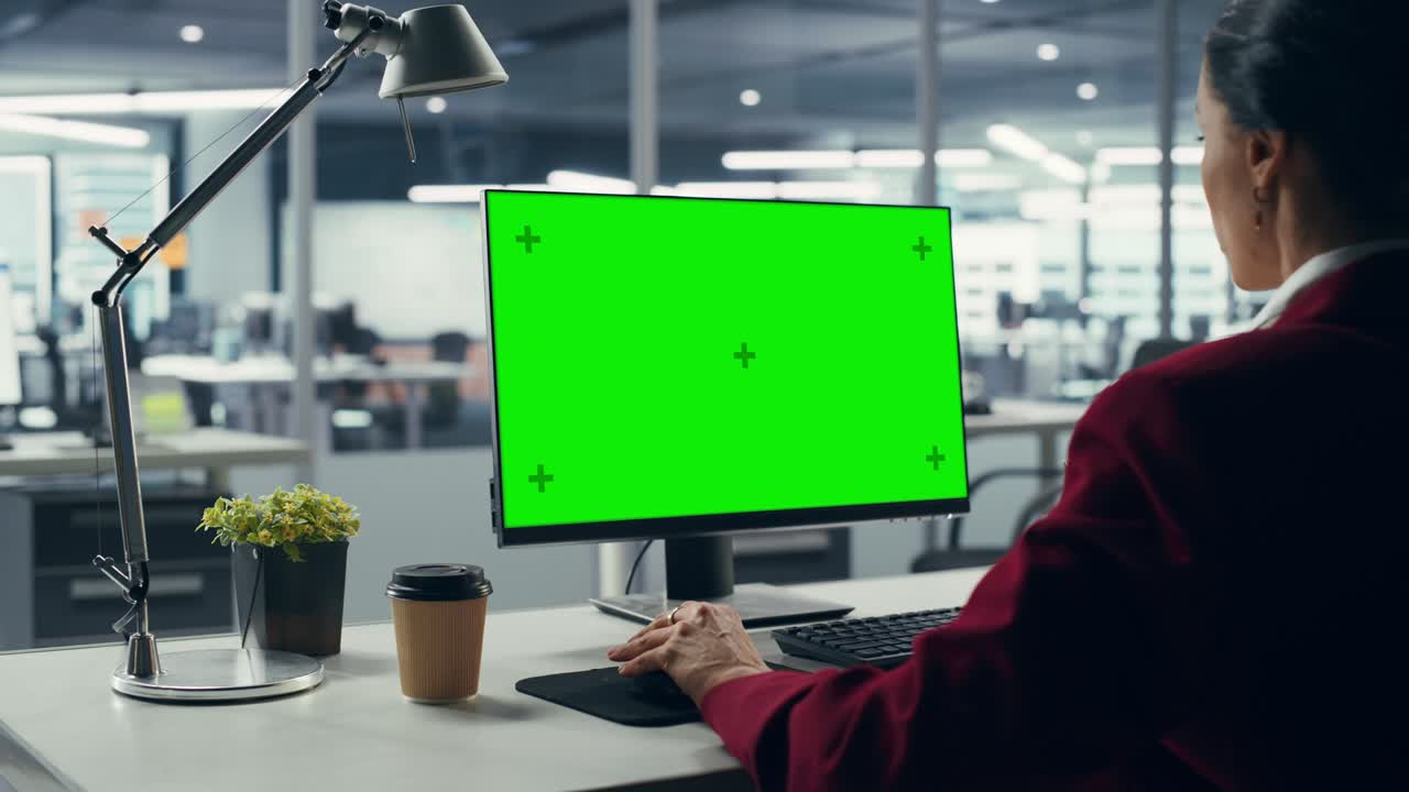 Successful Caucasian Businesswoman Sitting at Desk Working on Green Screen Laptop Computer in Office. Beautiful Businessperson using Chroma Key Display. Over Shoulder