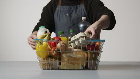 foto de estudio de un trabajador de la tienda revisando los alimentos básicos en la cesta de la compra de alambre del supermercado 1