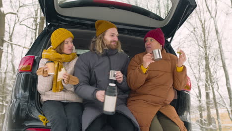 Drei-Freunde-Trinken-Und-Essen-Sandwich,-Während-Sie-Während-Einer-Winterreise-Im-Kofferraum-Sitzen