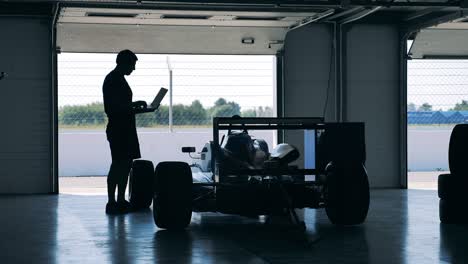 a mechanic with a laptop is checking a racing car