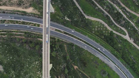 Train-passing-over-a-bridge-and-under-a-road-with-cars-in-a-green-area---Top-down-view