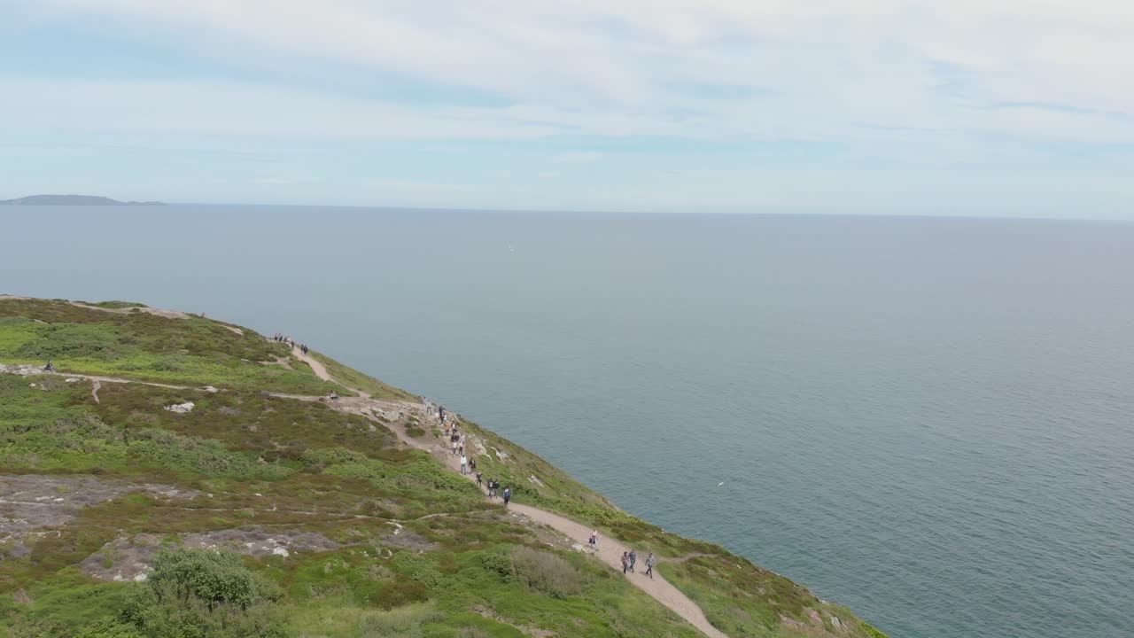 Droneflyvning af mennesker, der vandrer på et bjerg ved havet på en solrig dag