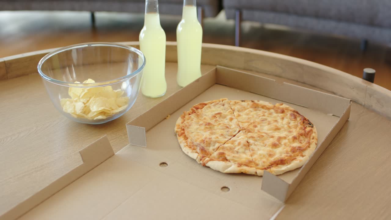I början rör sig kameran närmare över ett runt träbord och visar ostpizza, chips och lemonad