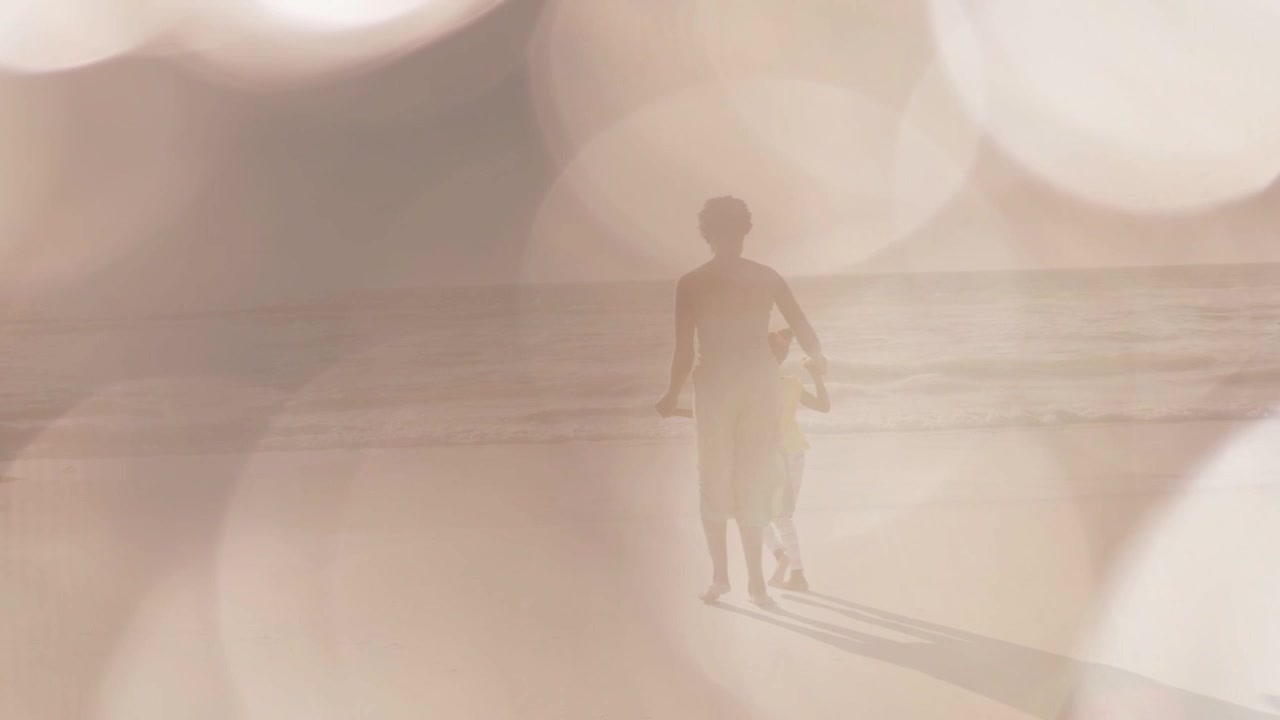 Mamma che crea un legame con il figlio camminando verso il mare, alzando il braccio per un abbraccio, con effetto bokeh in sovrapposizione per annunci