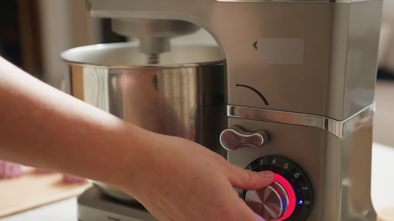 Close up of hand turning off electric mixer by adjusting speed dial with glowing red light, loosening mixer top and preparing to remove stainless steel mixing bowl during baking