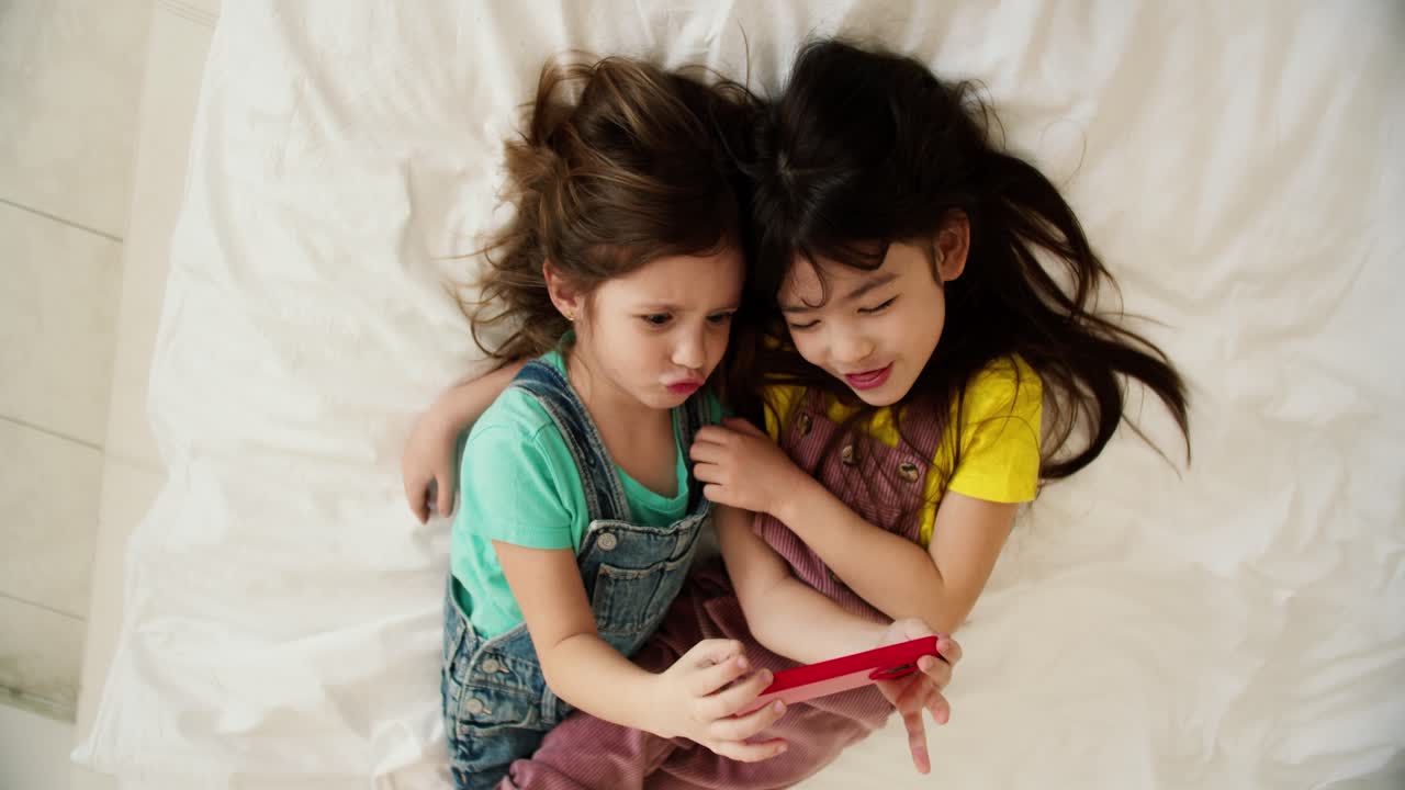 Two cute smiling preshool girls watching cartoons on smartphone, top view