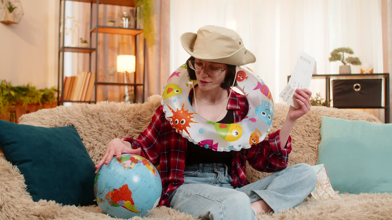 Woman planning beach vacation at home with inflatable swim ring holding globe and airplane tickets