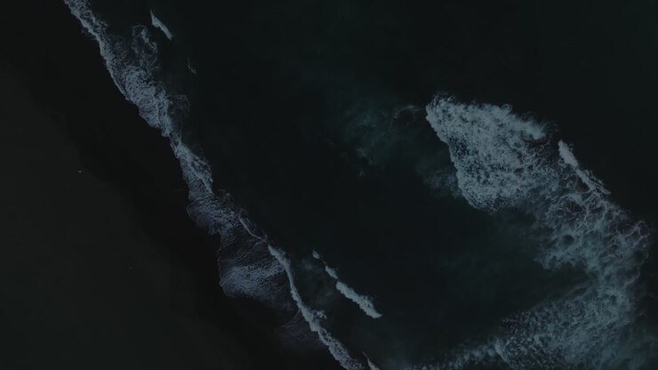Top down aerial footage of ocean waves breaking on black volcanic sand at Khalaktyrsky Beach, Kamchatka Krai, Russia, dramatic seascape background
